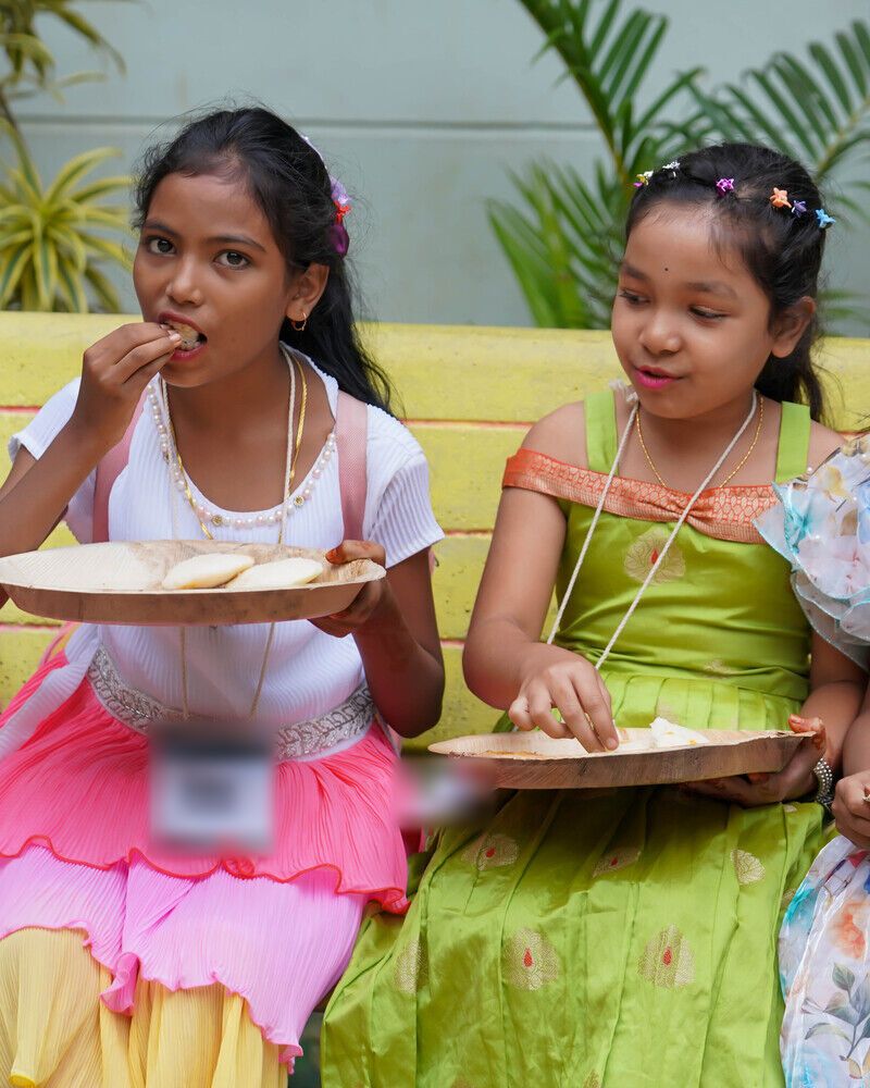 Two girls in festival dresses eating lunch on a bench at Kalakriti 2.0