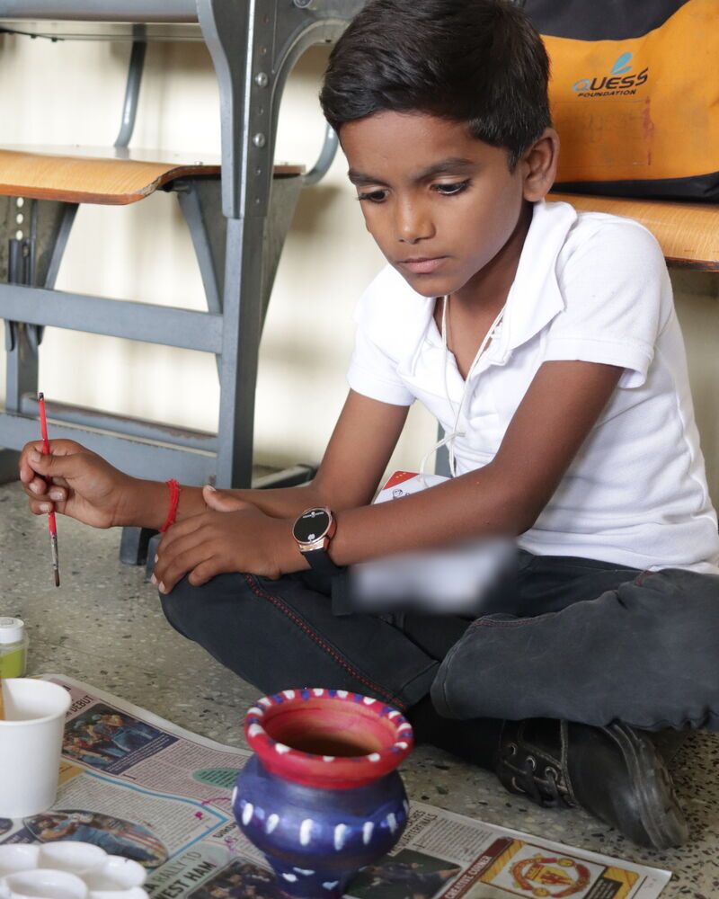 A boy painting a clay pot blue and red
