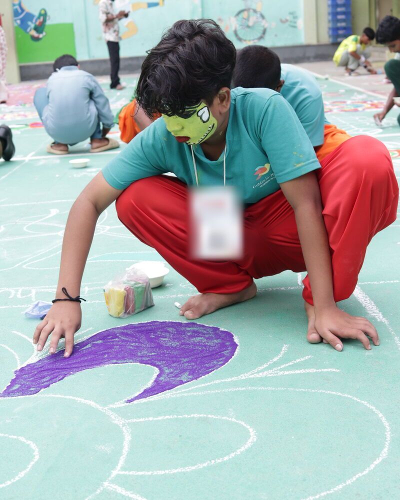 A boy crouching to draw a rangoli in chalk colours on the court